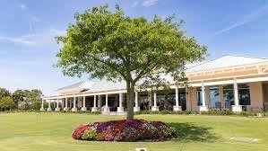 Clubhouse at Suntree Country Club in Suntree, Florida, featuring landscaped grounds, a large shade tree, colorful flower beds, and a manicured lawn.